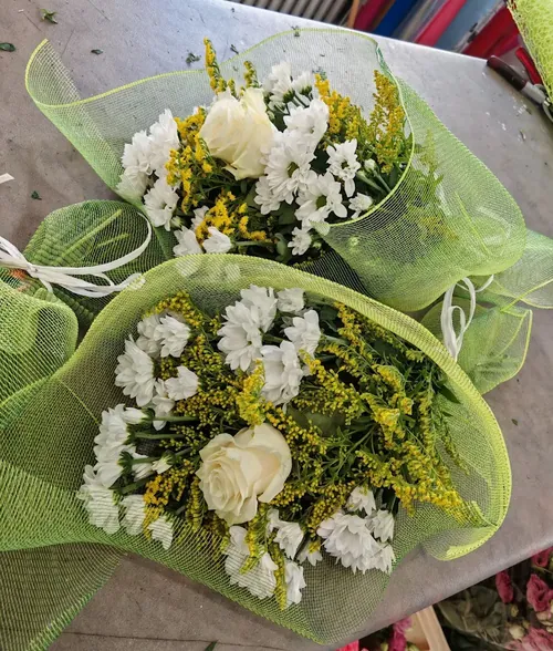 Due bouquet di rose bianche, margherite e solidago avvolti in rete verde sul banco di lavoro