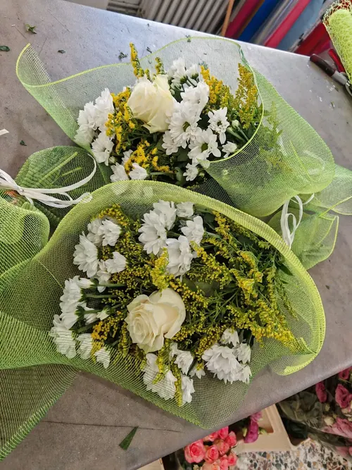 Due bouquet bianchi con rose, margherite e solidago in rete verde